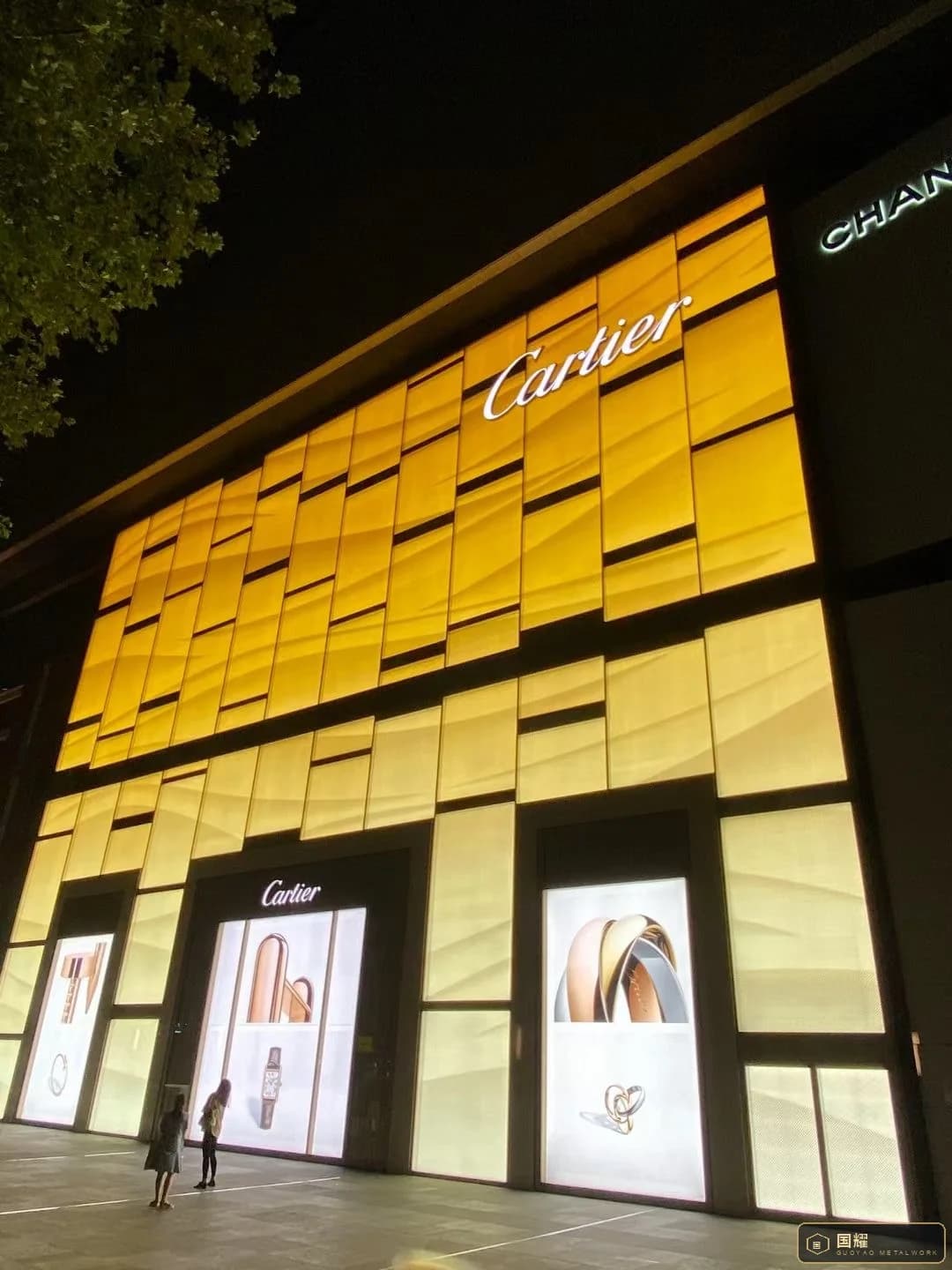 Cartier facade at night with the entire metal screen lit warm gold from behind
