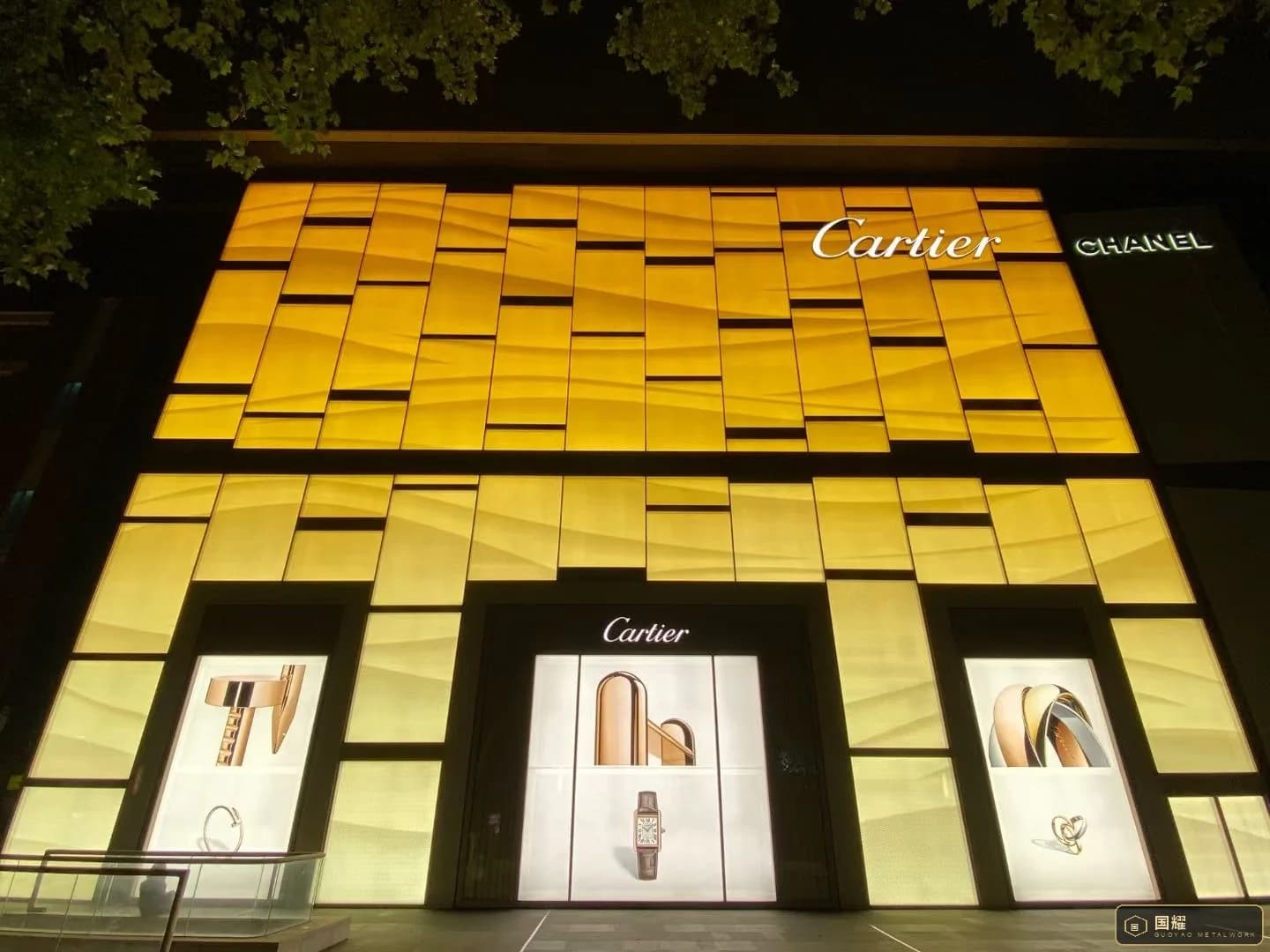 Close view of the illuminated Cartier facade showing panel joints and the three display windows at street level