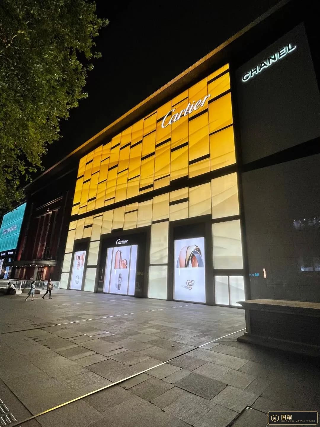 Cartier facade at night seen at an angle, showing the illuminated gold panels and the joint grid