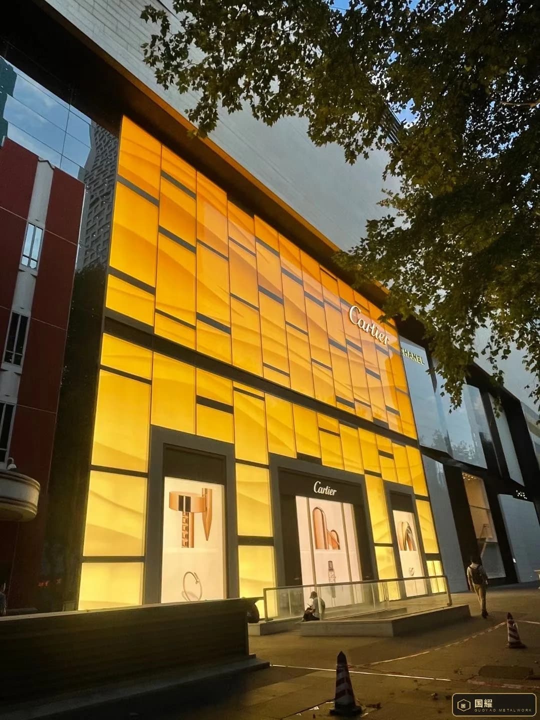 Cartier boutique facade at dusk, a backlit gold metal panel screen wrapping two storeys above the display windows