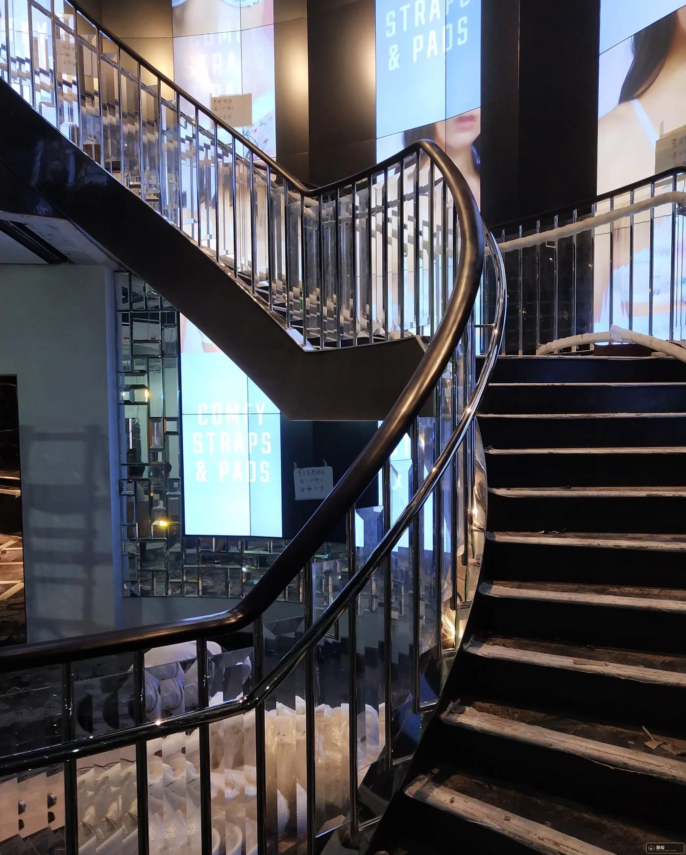 Finished helical staircase with black steel stringer, mirror stainless balustrade and continuous black handrail in a luxury retail store